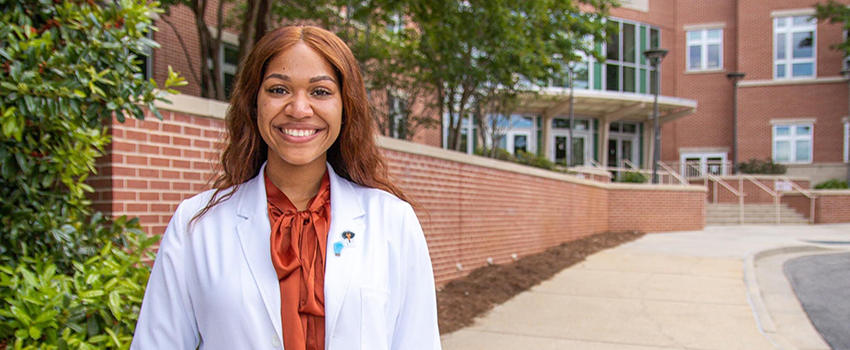 PT student T. Burns in front of Allied Health building in white coat.