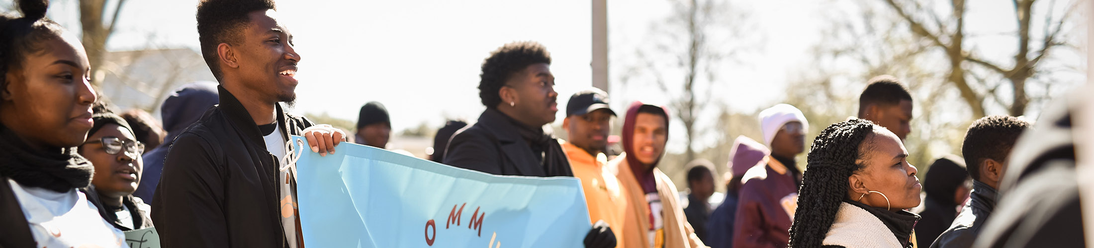 African American students marching in a parade carrying banner.