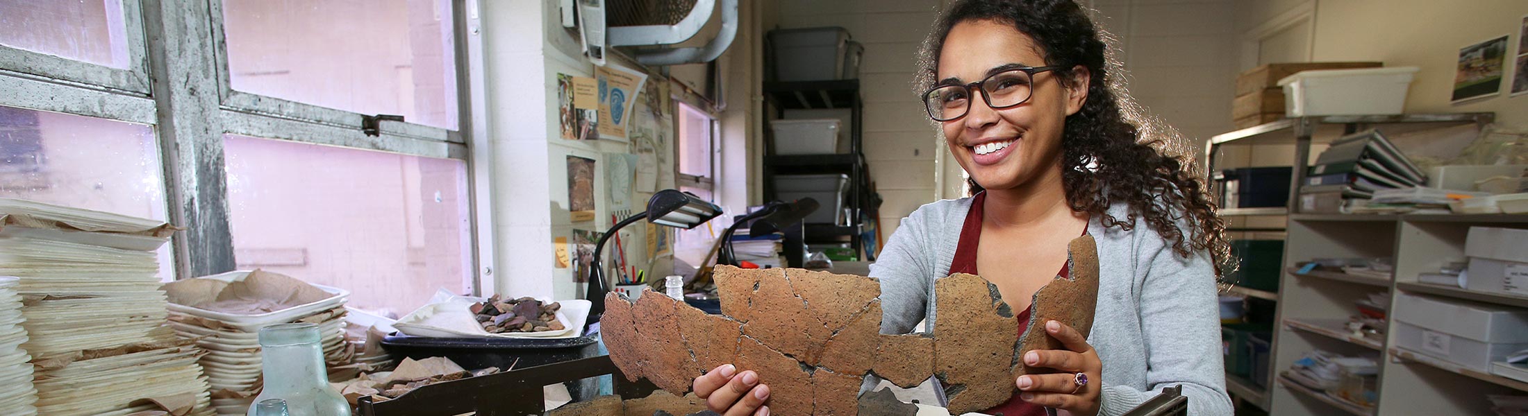 Student smiling holding up artifacts in lab.