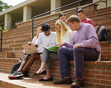 Students sitting at the amphitheater on campus looking at apapers and laptop.