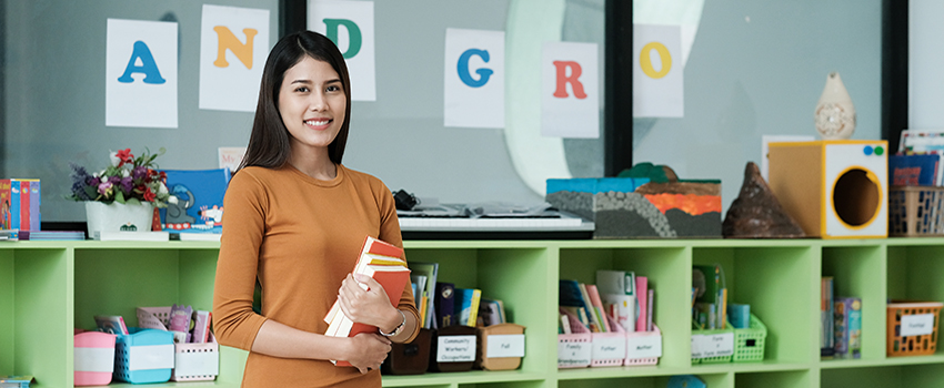 Teacher holding books in classroom.