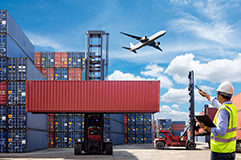 Man pointing toward airplane in the sky that is flying over shipping containers.