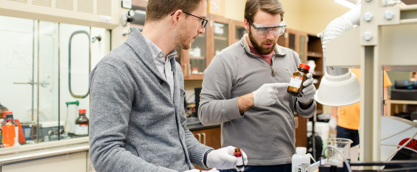 Two male students looking at bottle in lab.