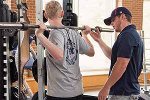 Student lifitng weights with another student assisting.