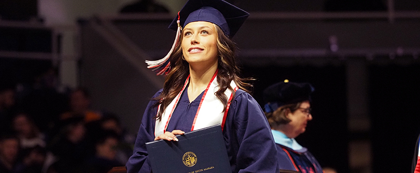 Graduate in cap and gown holding diploma.