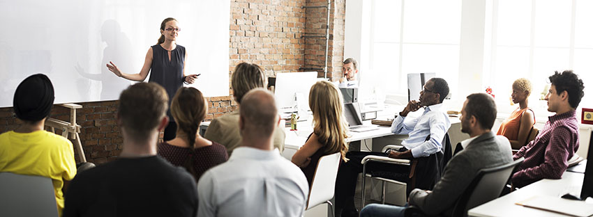 Woman teaching at white board in front of a group of people.