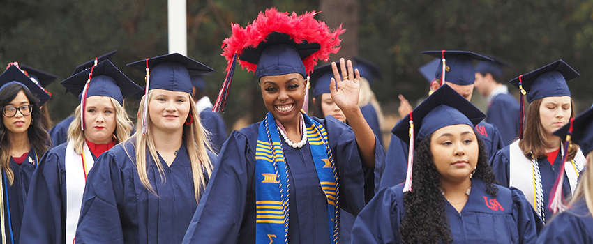 Student in cap and gown holding degree smiling