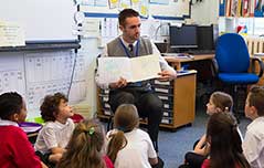 Male teacher reading a book to the class.