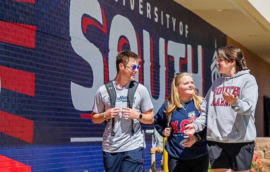 Three students walking and talking in front of mural outside of Student Center.